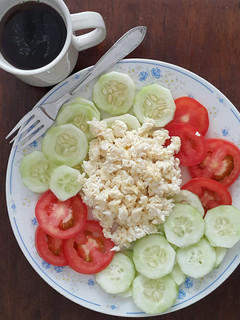 A picture of Scrambled eggs with tomato and cucumber salad.