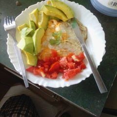 A picture of Fried egg garnished with avocado and tomatoes.