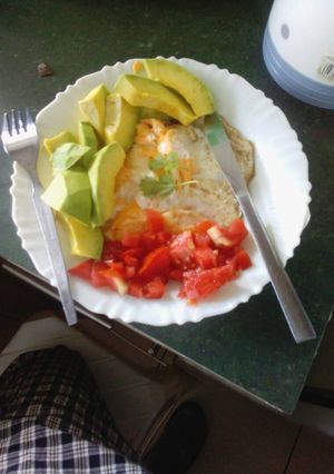 A picture of Fried egg garnished with avocado and tomatoes.