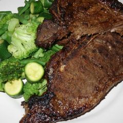 A picture of T bone steak with green vegetables.