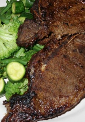 A picture of T bone steak with green vegetables.