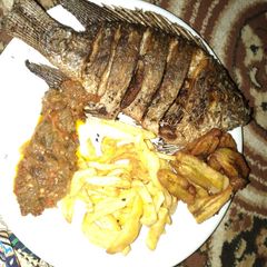 A picture of Fried tilapia fish with chips sauce and plantain.