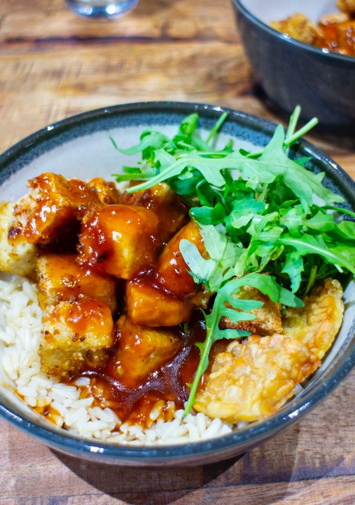 A picture of Crispy tofu top with sweet sticky and sour sauce with brown rice.