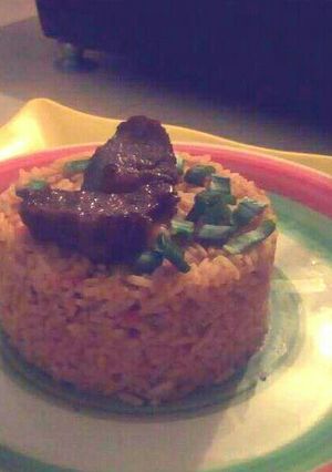 A picture of Jollof rice garnished with Beef and spring onions.