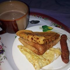 A picture of Pancakes, Fried Egg, Sausage with a cup of tea.