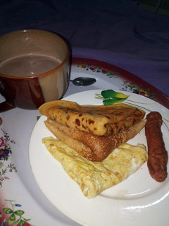 A picture of Pancakes, Fried Egg, Sausage with a cup of tea.