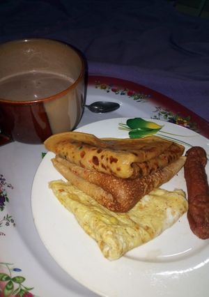 A picture of Pancakes, Fried Egg, Sausage with a cup of tea.