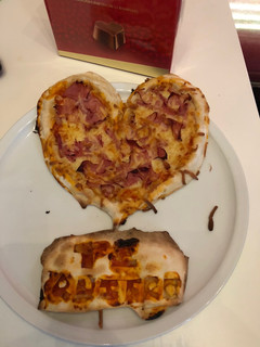 Una foto de Pizza de jamón y bacon con el borde relleno de queso de cabra con forma de corazón y tarjeta de masa