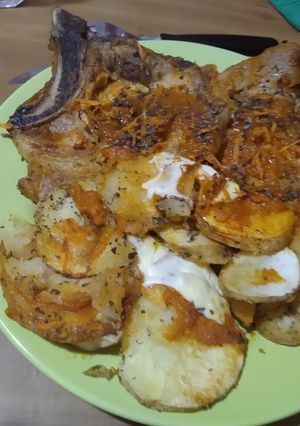 Una foto de Chuletas de cerdo, con papas al horno y salsa de ajo y cebolla