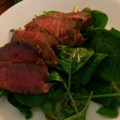 A picture of London broil over spinach salad.