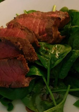 A picture of London broil over spinach salad.