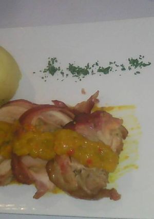 Una foto de Involtini de pollo relleno con jamón y queso albardado con tocineta y puré liso con salsa chutney de mango