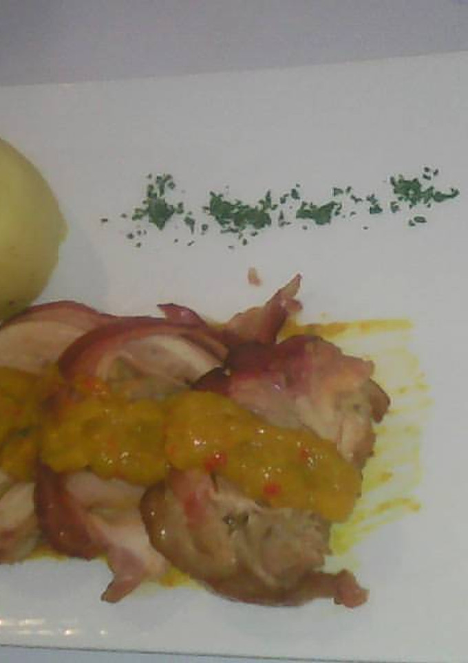 Una foto de Involtini de pollo relleno con jamón y queso albardado con tocineta y puré liso con salsa chutney de mango