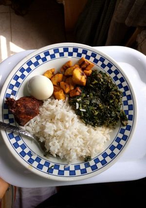 A picture of White rice with vegetable, peppered chicken, boiled egg and diced plantain.