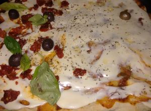 Una foto de Pizza mitad con tomates secos y albahaca