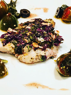 Una foto de Pescado en Costra de Semillas y Aceitunas Negras, acompañado de Uvalinas y Aceitunas en Ensalada