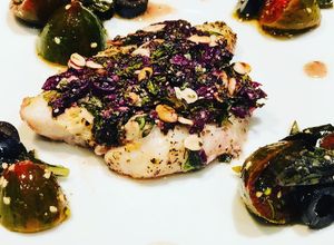 Una foto de Pescado en Costra de Semillas y Aceitunas Negras, acompañado de Uvalinas y Aceitunas en Ensalada