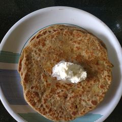 A picture of Aloo pyaz Paratha with white butter.
