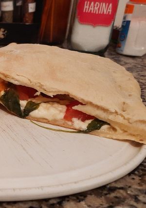 Una foto de Calzone de queso, tomate y rúcula
