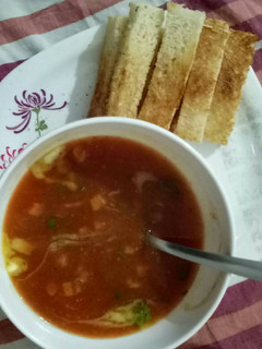 A picture of Tomato and carrot soup with bread sticks.