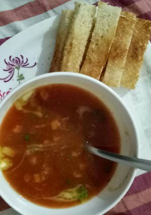 A picture of Tomato and carrot soup with bread sticks.