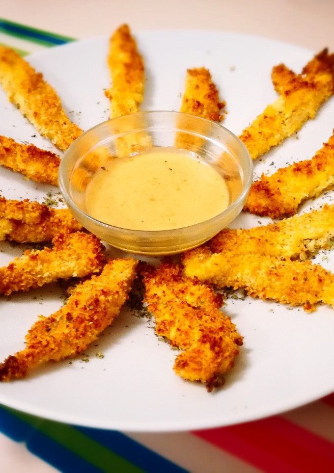 Una foto de Delicias de pollo crujiente con rebozado de panko y parmesano, acompañadas de salsa miel y mostaza