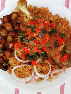 A picture of Jollof rice and fried chicken sauce garnished with plantain.