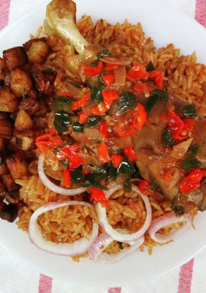 A picture of Jollof rice and fried chicken sauce garnished with plantain.
