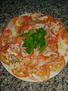 Una foto de Carpaccio de tomate con parmesano y albahaca