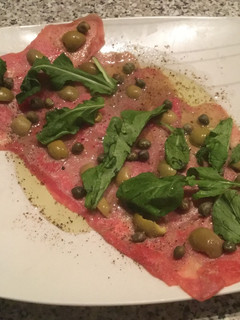 Una foto de Carpaccio con aceitunas y rúcula