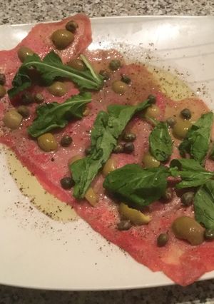 Una foto de Carpaccio con aceitunas y rúcula