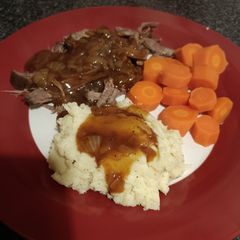 A picture of Slow cooked beef brisket, mash carrots and onion gravy.