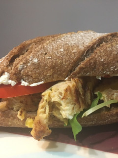 Una foto de Bocatín de tortilla de calabacín y cebolla caramelizada con queso crema, tomate y rúcula