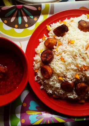 A picture of Boiled rice with tomato sauce and fried plantain.