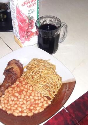 A picture of Spaghetti jollof with Baked Beans on the side.