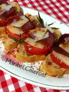 Una foto de Canapés de pan de aceitunas, tomate, queso y mojama de atún
