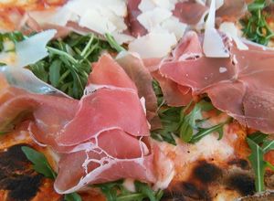 Una foto de Pizza de prosciutto, rúcula y parmesano
