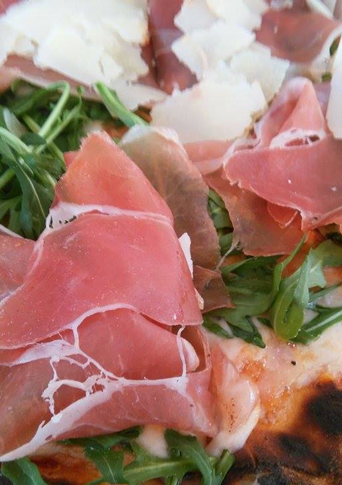 Una foto de Pizza de prosciutto, rúcula y parmesano