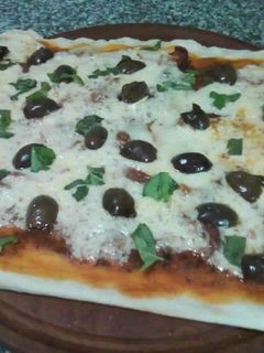 Una foto de Pizza de jamón crudo, aceitunas negras y albahaca