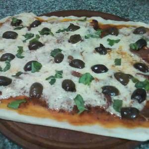Pizza de jamón crudo, aceitunas negras y albahaca