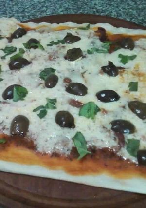 Una foto de Pizza de jamón crudo, aceitunas negras y albahaca