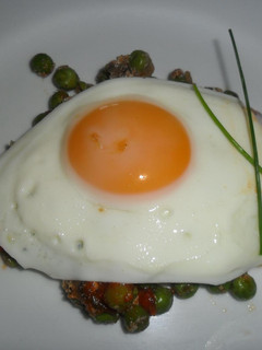 Una foto de Huevo frito sobre colchón de arvejas