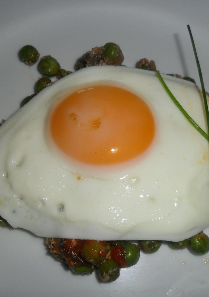 Una foto de Huevo frito sobre colchón de arvejas