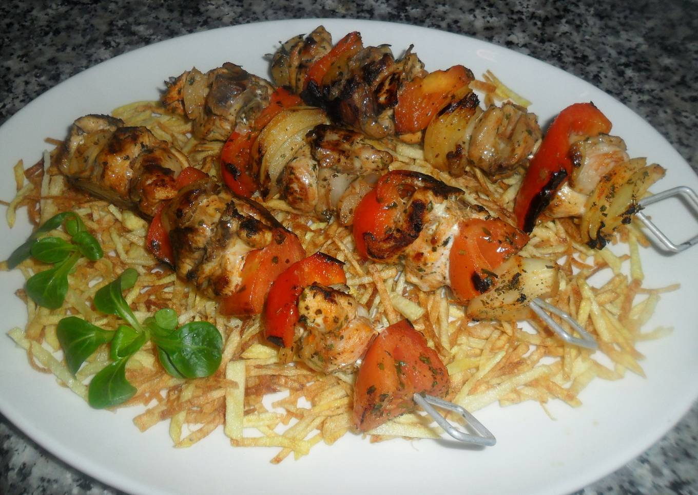 Brochetas de pollo sobre patatas paja<br />