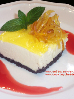 Una foto de Cheesecake de chocolate blanco y limón con coulis de frutillas y cáscaras confitadas de cítricos